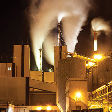 Beleuchtete Papierfabrik bei Nacht. In Papierfabriken wird Natriumsulfit als Sauerstoffbindemittel verwendet, um Wasser aufzubereiten, das Dampfkesseln zugeführt wird. So wird Korrosion vorgebeugt.